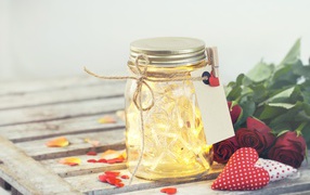 Стеклянная банка с гирляндой на столе с букетом роз и сердечками