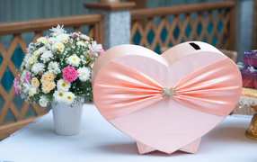 Large pink box in the shape of a heart on a table with a bouquet of chrysanthemums