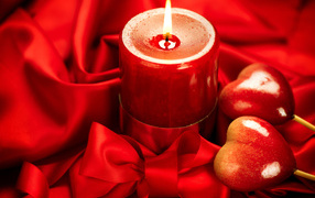 Lighted candle with two hearts on a red background with a bow