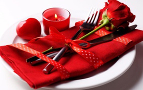 Роза, столовые приборы и зажженная свеча на белой тарелке 