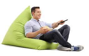 Мужчина с попкорном и пультом от телевизора лежит на зеленой подушке