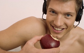 Красивый голубоглазый парень в наушниках с яблоком в руке