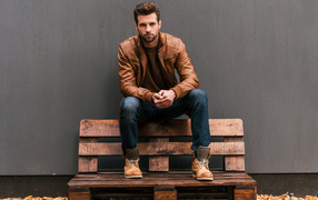 Молодой красивый мужчина сидит на деревянной лавке