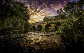 Зеленые ивы на берегу реки у старого моста под красивым небом