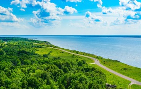 Дорога через побережье вдоль моря под голубым небом с белыми облаками