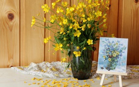 Букет желтых полевых лютиков в стеклянной вазе на столе с картиной