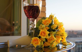 A bouquet of yellow roses on a table with a glass of wine
