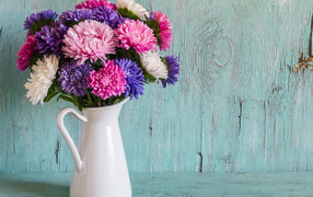 Разноцветные астры в вазе на деревянном фоне