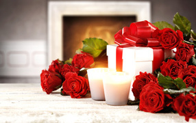 Красные розы с подарком и двумя зажженными свечами на столе
