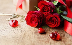 Три красных розы на деревянном столе с красными сердечками