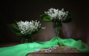 Два букета ландышей с бусами на столе 