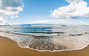 Морская волна на песке под красивым небом с белыми облаками