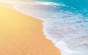 Белые волны голубого океана на желтом песке 