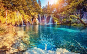 Водопад в лучах солнца стекает со скалы в реку