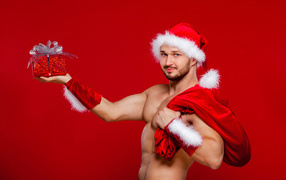 Мужчина в новогоднем костюме Санта Клауса с мешком и подарком в руке на красном фоне