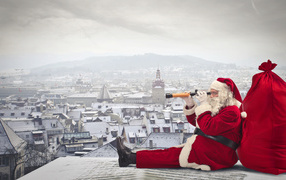 Санта Клаус сидит на крыше дома с большим красным мешком