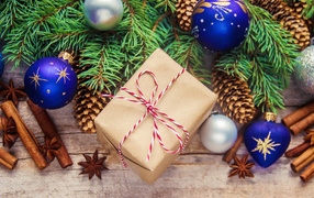 Еловая ветка с игрушками на столе с корицей и подарком на Новый год 