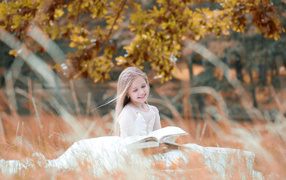 A girl in a beautiful white dress is reading a book in the nature