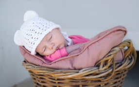 Маленький ребенок в белой шапке спит в корзине