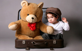 Маленький мальчик сидит в чемодане с плюшевым мишкой 