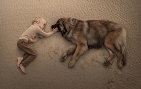 Маленький мальчик лежит на песке с большой собакой