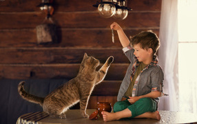 Маленький мальчик дразнит рыбой серого кота