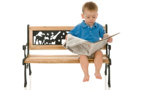 A little boy with a newspaper is sitting on a bench