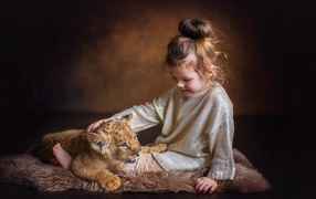 A little girl is petting a little lion cub