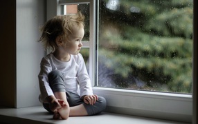 Маленькая девочка сидит на подоконнике у окна