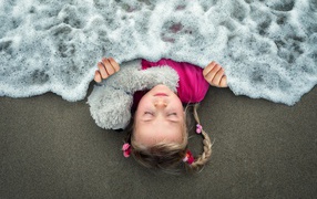Маленькая девочка спит на песке под одеялом из морской пены