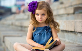 Маленькая девочка с цветком в волосах сидит на ступенях