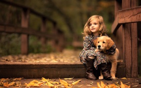 A little girl with a golden retriever sits on a bridge