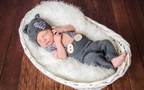 Спящий младенец в сером костюме в белой корзине