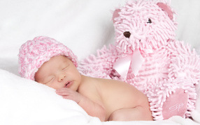 Спящий грудной ребенок в шапке с большим розовым медведем