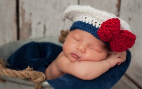 Спящий грудной ребенок в вязаной шапочке с красным бантом