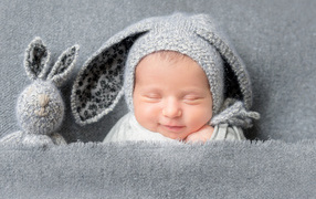 Маленький грудной ребенок в серой шапке с ушками