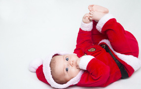 Маленький ребенок в красном новогоднем костюме на сером фоне