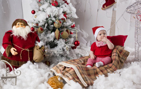 Маленький ребенок в санях у елки с дедом морозом на Новый год 