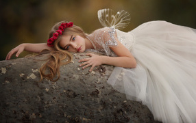 Красивая маленькая девочка в белом платье лежит на камне