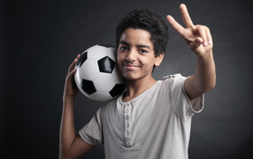 Мальчик с футбольным мячом на плече на сером фоне