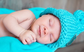 Милый спящий ребенок в голубой вязаной шапке