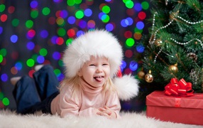 Смешная девочка в новогодней шапке у елки