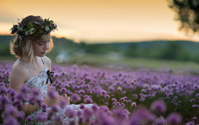 Gentle little girl sits on the field with lilac flowers