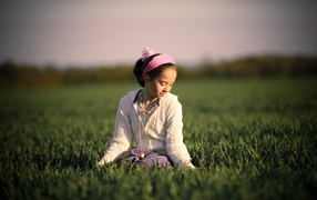 Девочка с розовой повязкой на голове сидит в зеленой траве