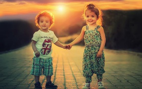 Счастливые мальчик и девочка на дороге на фоне заката