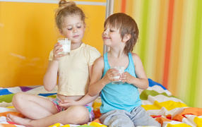 Маленькие мальчик и девочка со стаканами молока в руках 