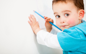 Маленький мальчик рисует карандашом на стене