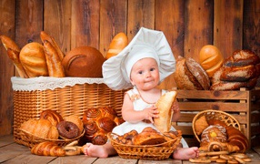 Маленький мальчик в костюме повара сидит на столе с выпечкой