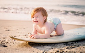 Маленький мальчик на доске для серфинга на пляже