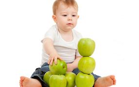 Little boy playing with green apples on white background